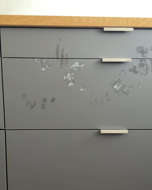 Graue Matt-Schubladen mit Eichen-Arbeitsplatte, darauf Handabdrücke und Fingertapser